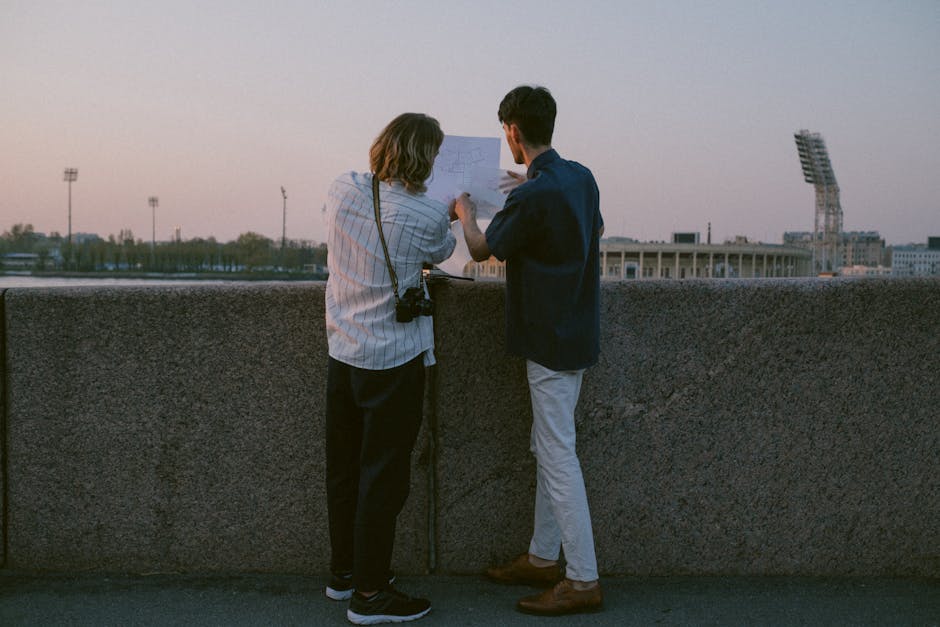 Two individuals review architectural plans outdoors at sunset with a cityscape view.